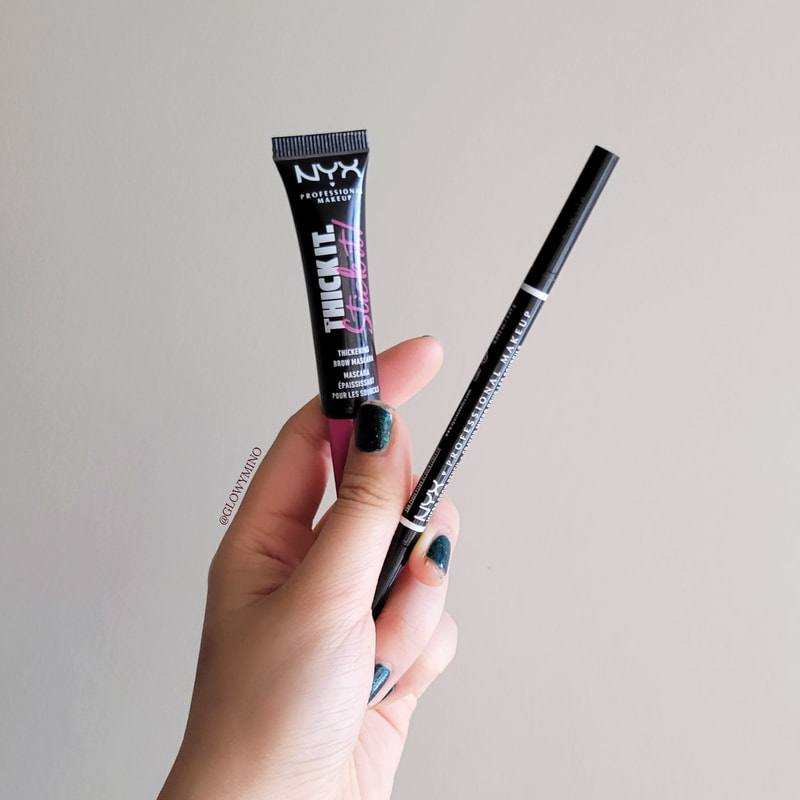 a hand holding up a brow gel and brow pencil against a gray background