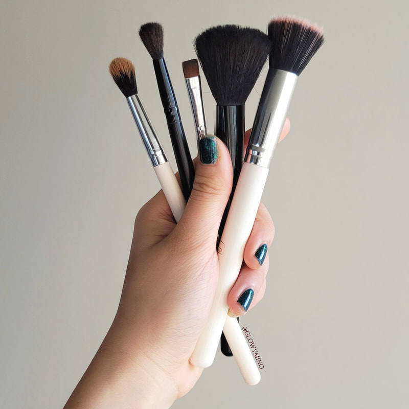 holding 5 makeup brushes against a gray background